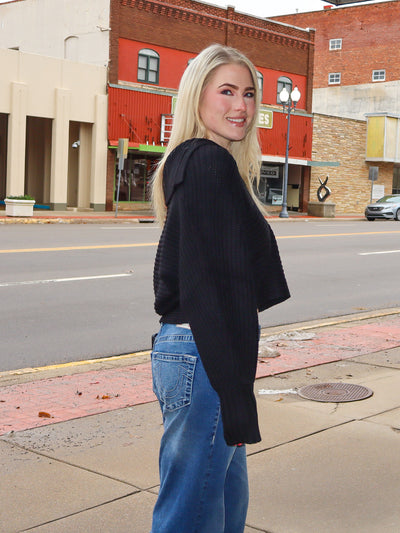 Model is wearing a black V neck sweater with blue jeans.  