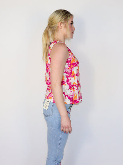 Model is wearing light pink, white, and hot pink leaf printed sleeveless top. Top has slits on the bottom on both sides. Worn with blue jeans.