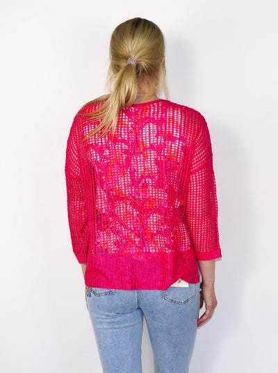 Model is wearing a hot pink fishnet crochet sweater. Sweater is paired with a floral tank top underneath and blue jeans. 
