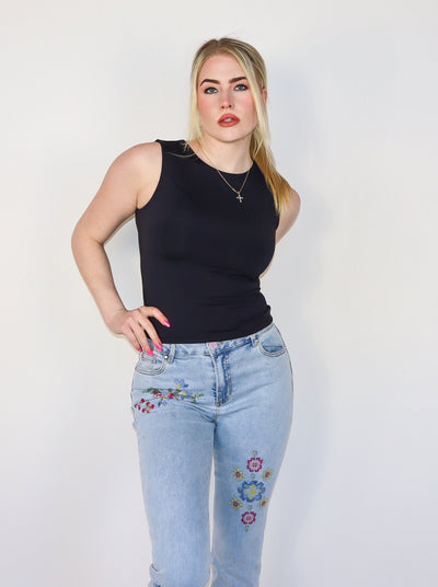 Model is wearing a fitted black crew neck tank top. Top is paired with blue jeans. 