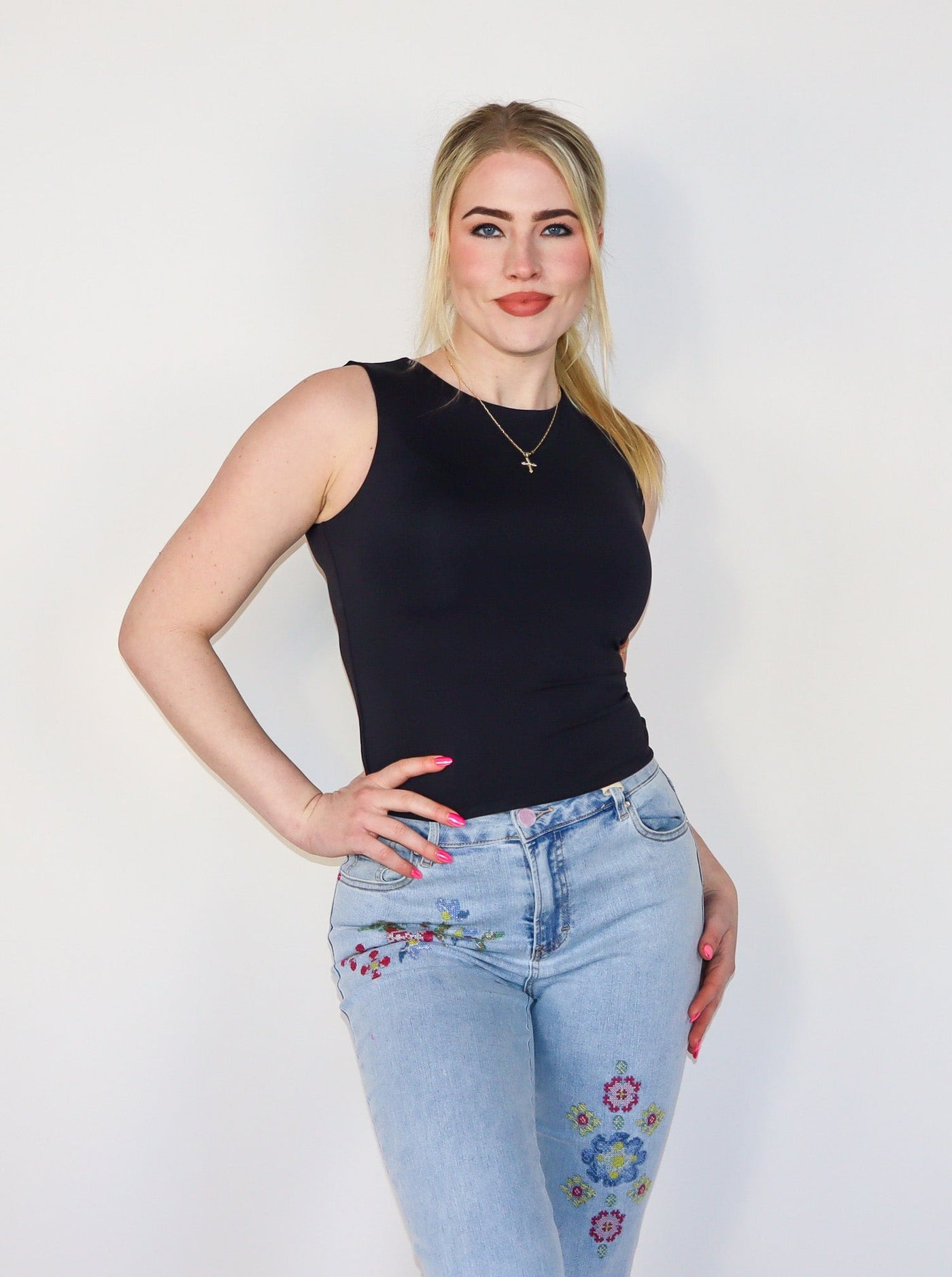 Model is wearing a fitted black crew neck tank top. Top is paired with blue jeans.