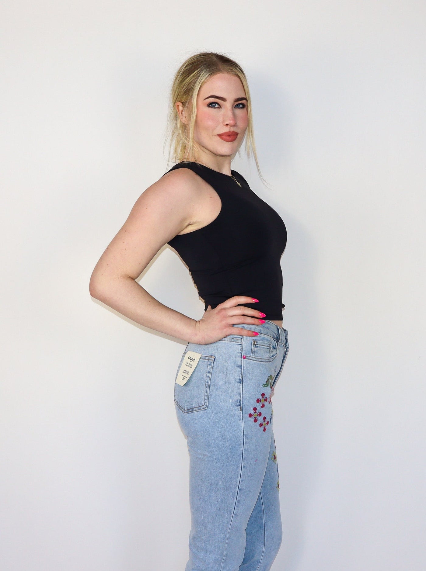 Model is wearing a fitted black crew neck tank top. Top is paired with blue jeans.