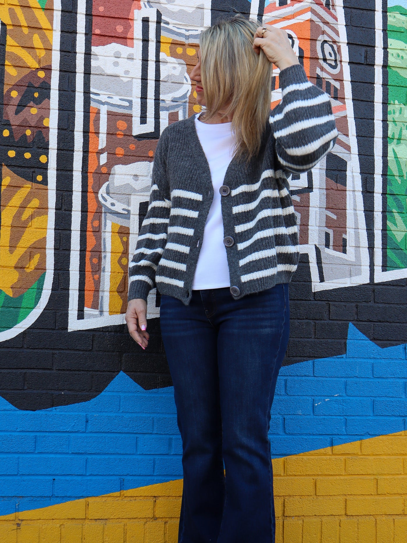 Model is wearing a grey and white button up striped cardigan. Cardigan is paired with a white top and blue jeans. 