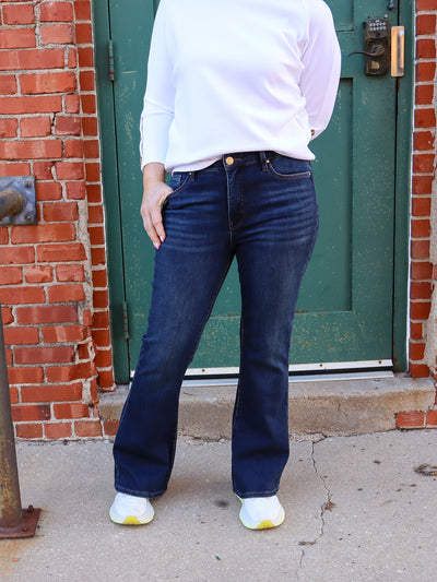 Model is wearing dark wash flare high rise blue jeans paired with a white top and white sneakers. 