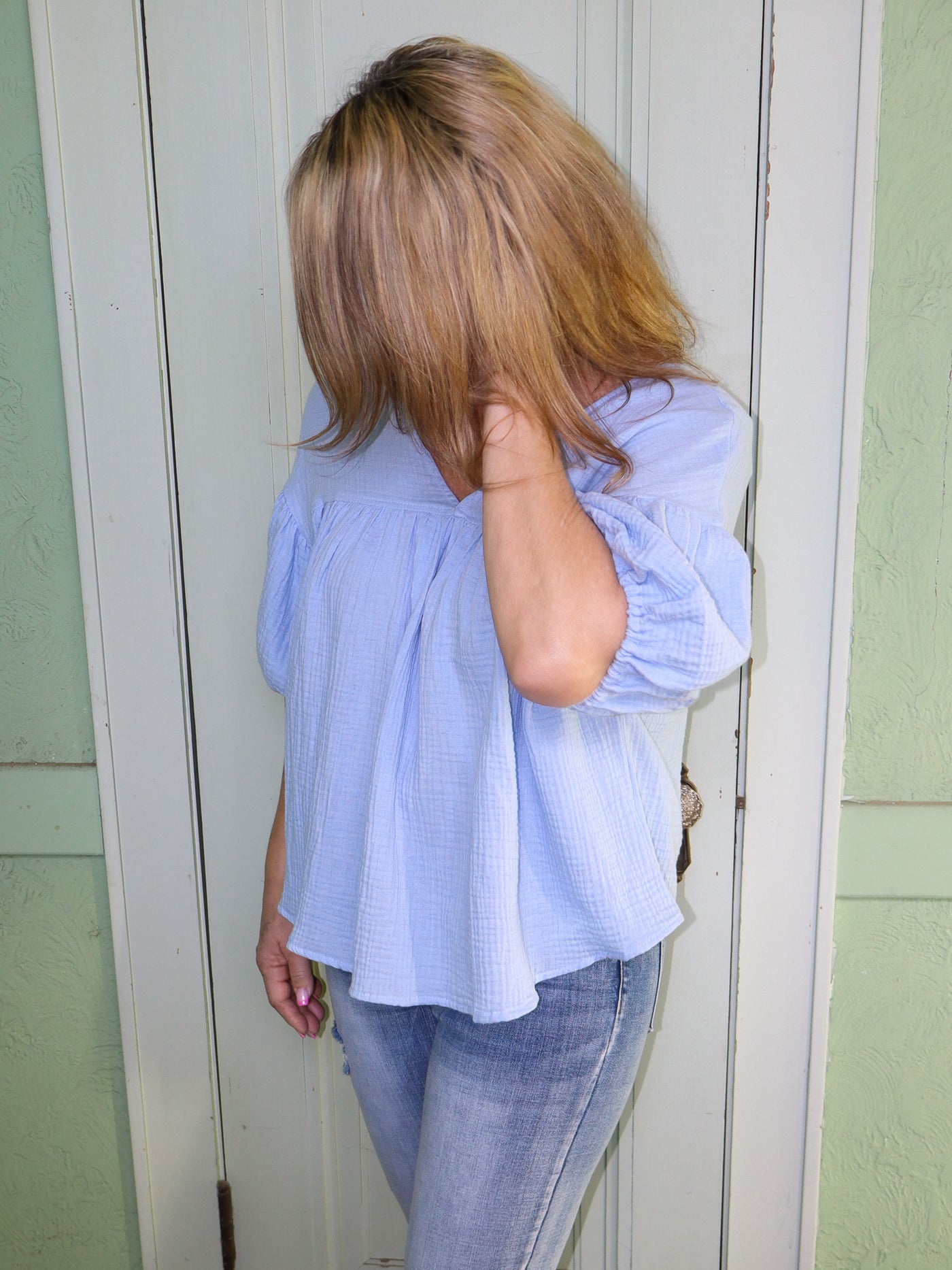 Model is wearing a baby blue baby doll style top with a v-neck. Top is paired with blue jeans. 