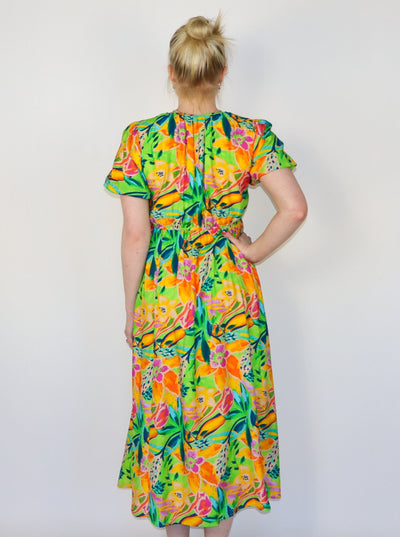 Model is wearing a flowy multi colored midi dress with puffy sleeves, a vneck, and string detail on the neckline. Dress is paired with white tennis shoes. 