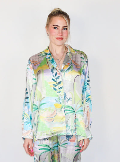 Model is wearing a silky button up collared blouse with a beachy/summery print. Top is paired with matching bottoms. 