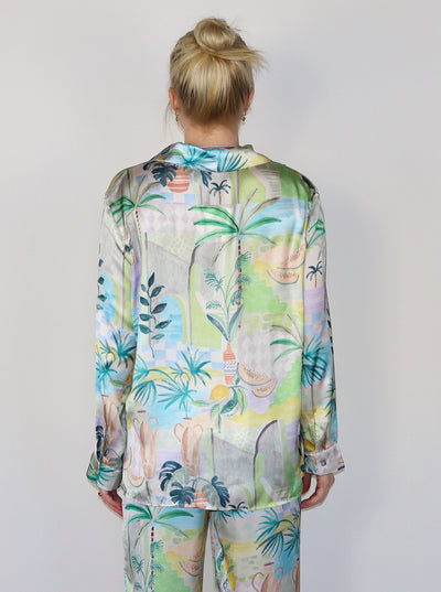 Model is wearing a silky button up collared blouse with a beachy/summery print. Top is paired with matching bottoms.