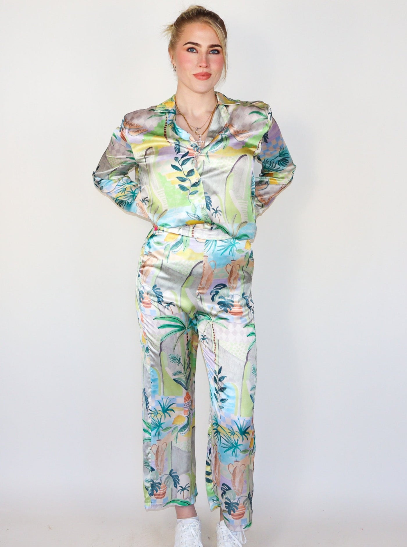 Model is wearing a high waisted multi colored printed pant that is silky material. Pants are paired with a matching top and white sneakers. 