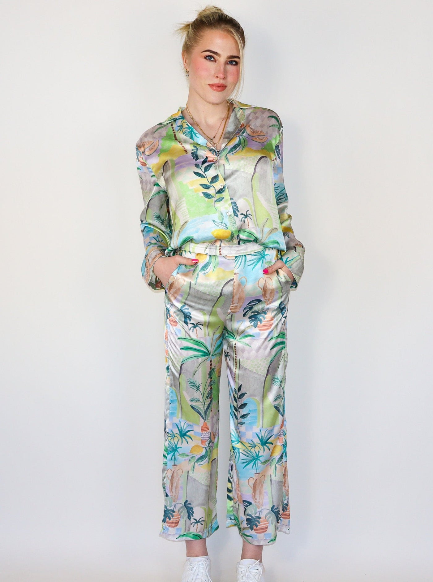 Model is wearing a high waisted multi colored printed pant that is silky material. Pants are paired with a matching top and white sneakers.