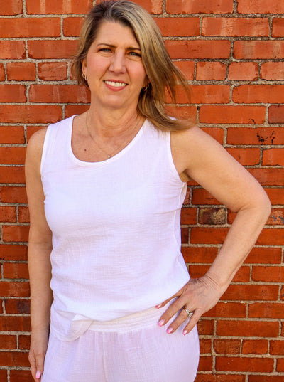 Model is wearing a light weight white tank top with thick straps. Tank is paired with white pants. 