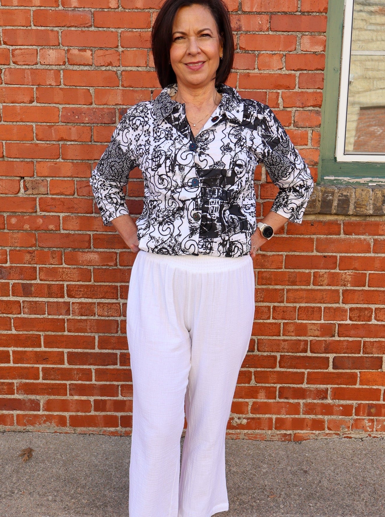 Model is wearing flowy white cotton pants that have a breathable material and a thick waist band. Pants are worn with a black and white blouse. 