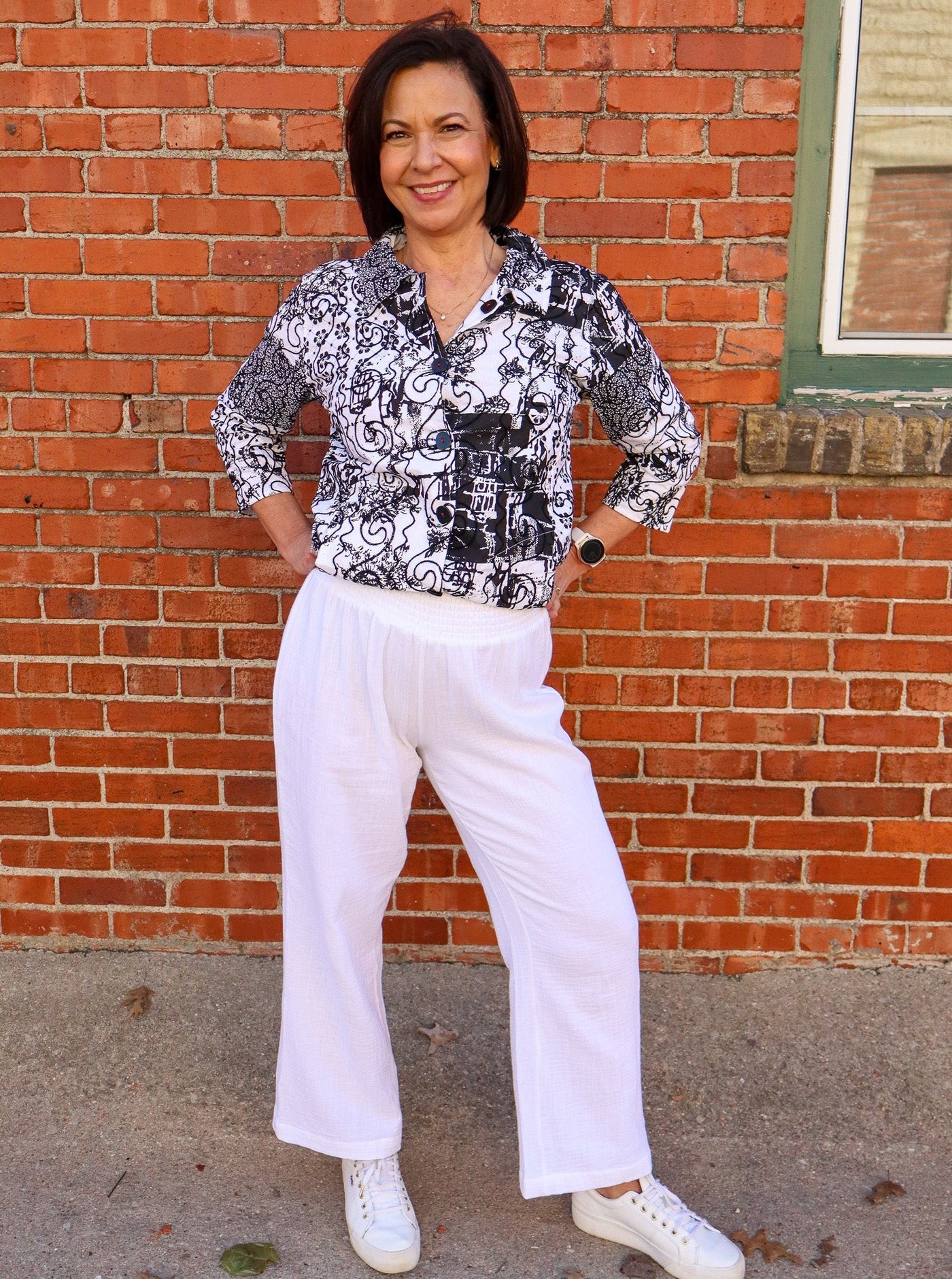 Model is wearing flowy white cotton pants that have a breathable material and a thick waist band. Pants are worn with a black and white blouse. 