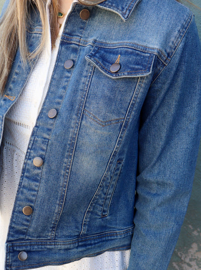 Model is wearing a dark wash blue jean jacket Jean jacket is worn with a white mini dress and sandals. 