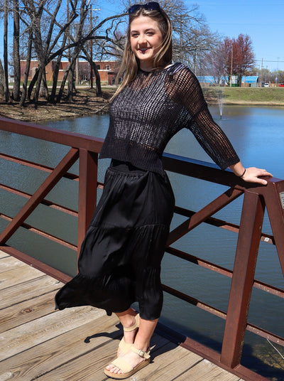 Model is wearing a black tiered maxi skirt. Maxi is paired a white tank and knitted black sweater