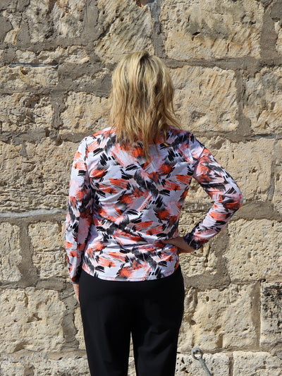 Model is wearing a black and orange abstract printed fitted active wear quarter zip. Paired with black pants.