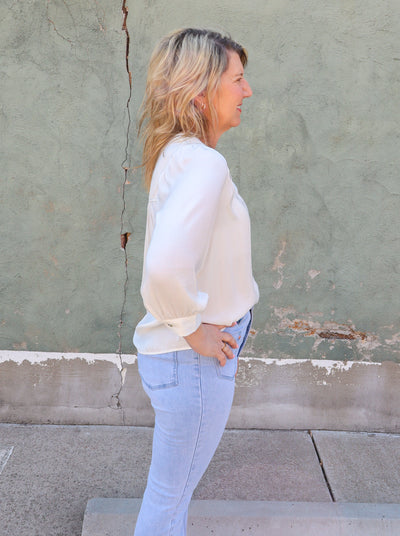 Model is wearing a long sleeve cream colored v-neck blouse. Paired with blue jeans.
