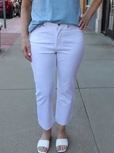 Model is wearing a white straight leg ankle length denim jean with a distressed hem at the ankle.