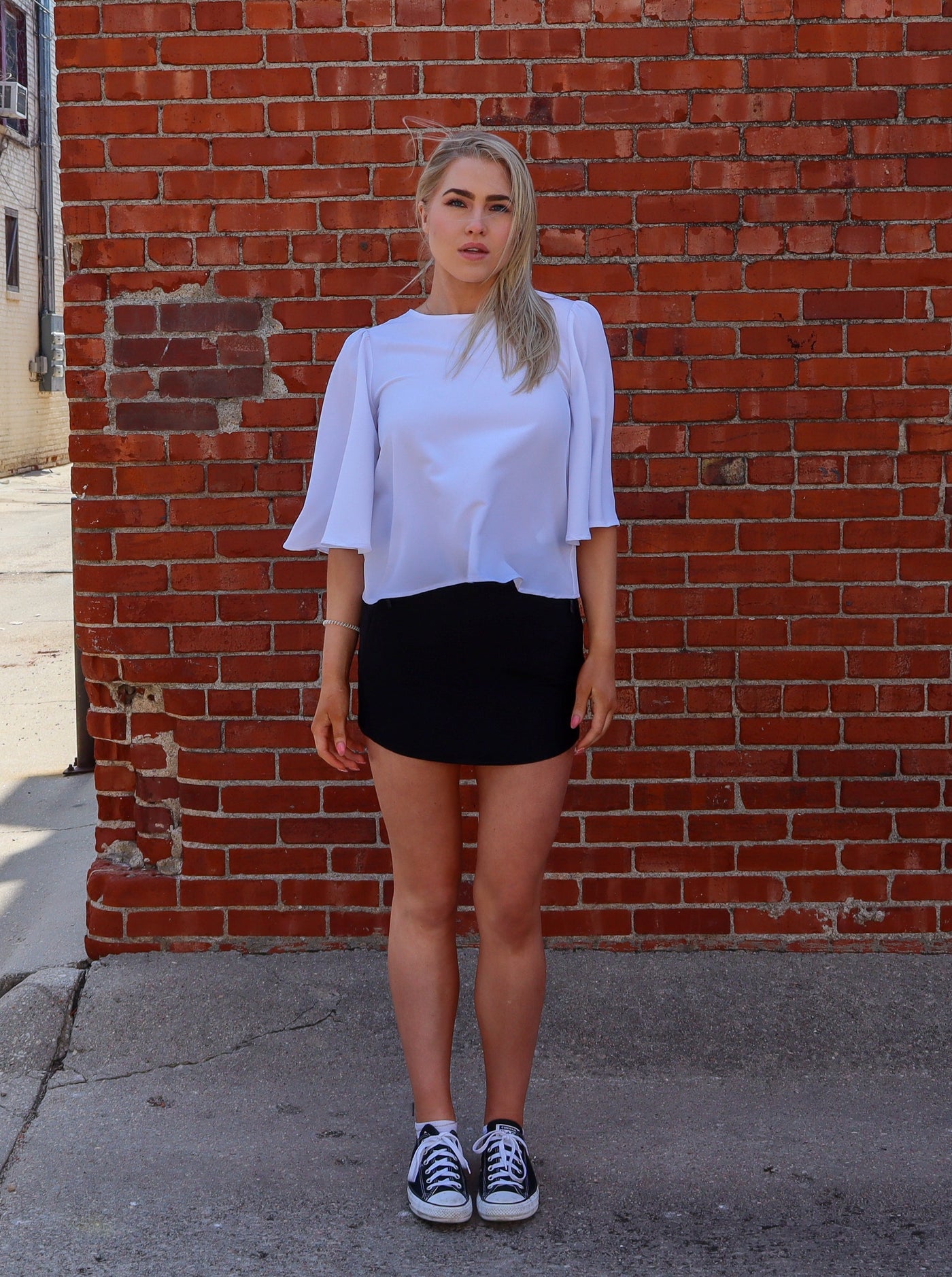 Model is wearing a half sleeve flutter sleeve white blouse, paired with a black tennis skirt.