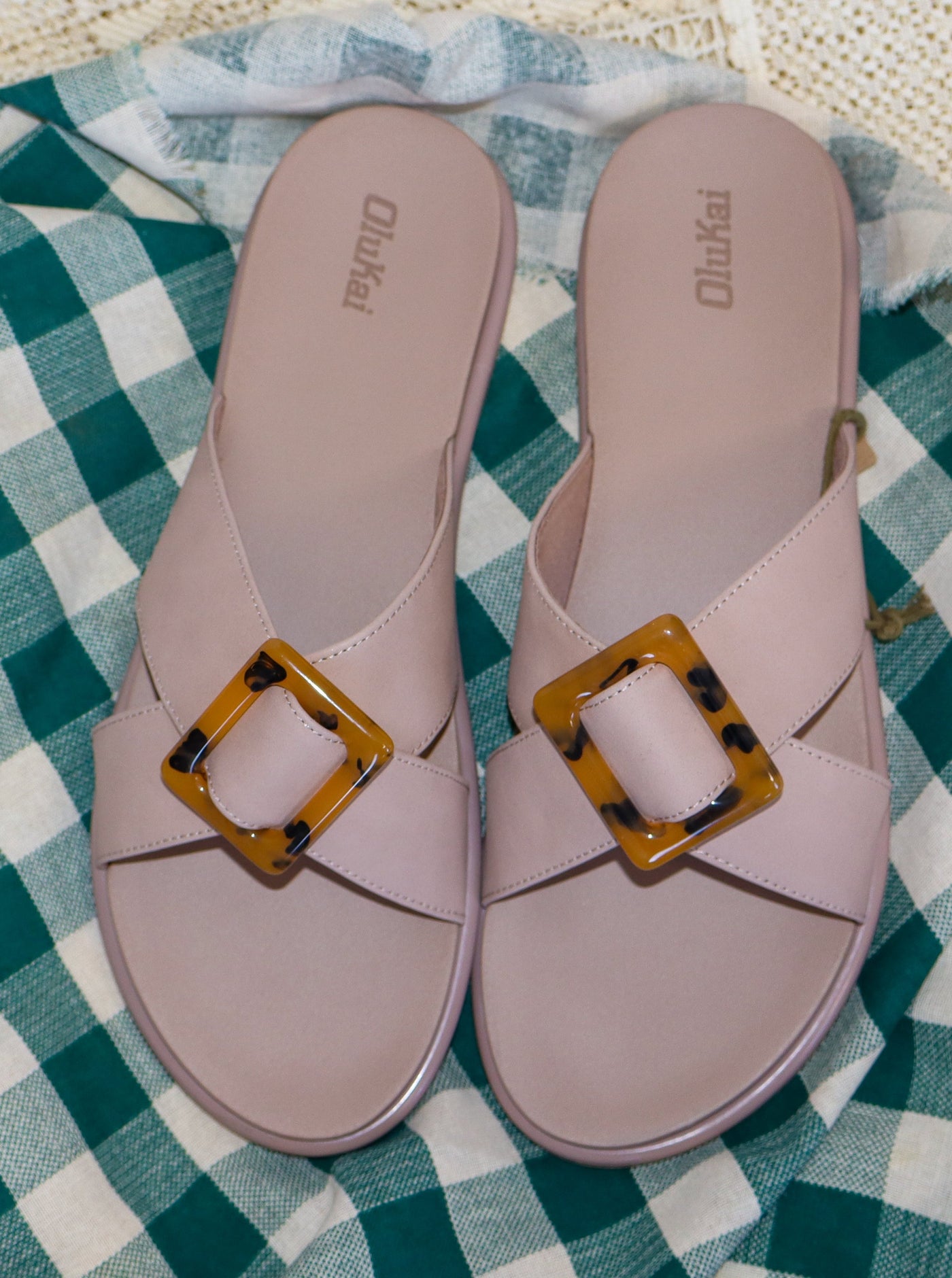 OluKai Taupe colored sandals with a tortoise clasp on the straps on top of the sandal.