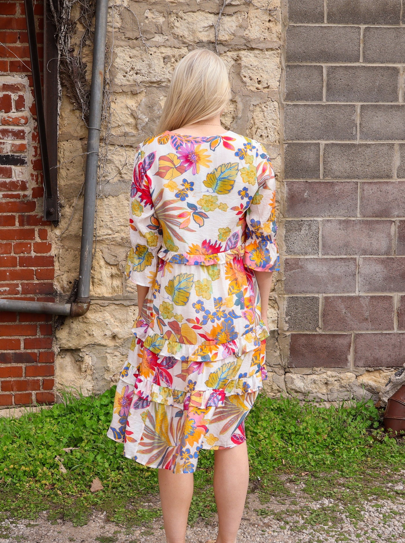 Model is wearing a half sleeve multi colored and white ruffled v-neck floral midi dress paired with beige sandals.