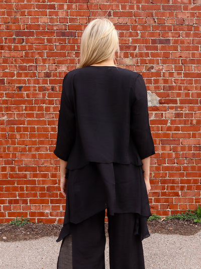 Model is wearing a long open flowy black half sleeve blouse. Paired with matching pants and sandals.