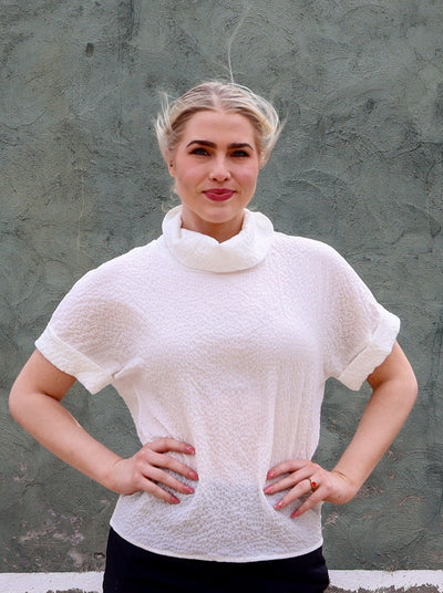 Model is wearing a collared high neck short sleeve cream textured blouse.