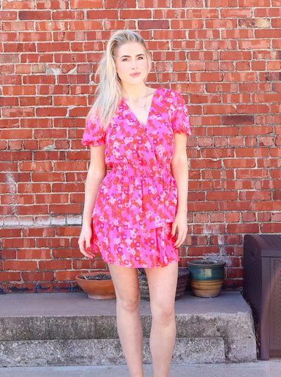 Model is wearing a floral pink ruffle mini dress with short sleeves and a deep neckline.