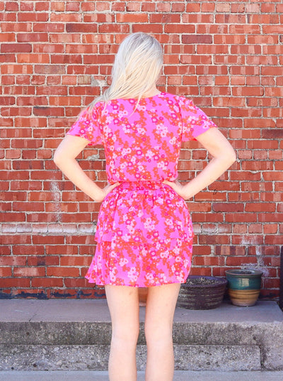 Model is wearing a floral pink ruffle mini dress with short sleeves and a deep neckline.
