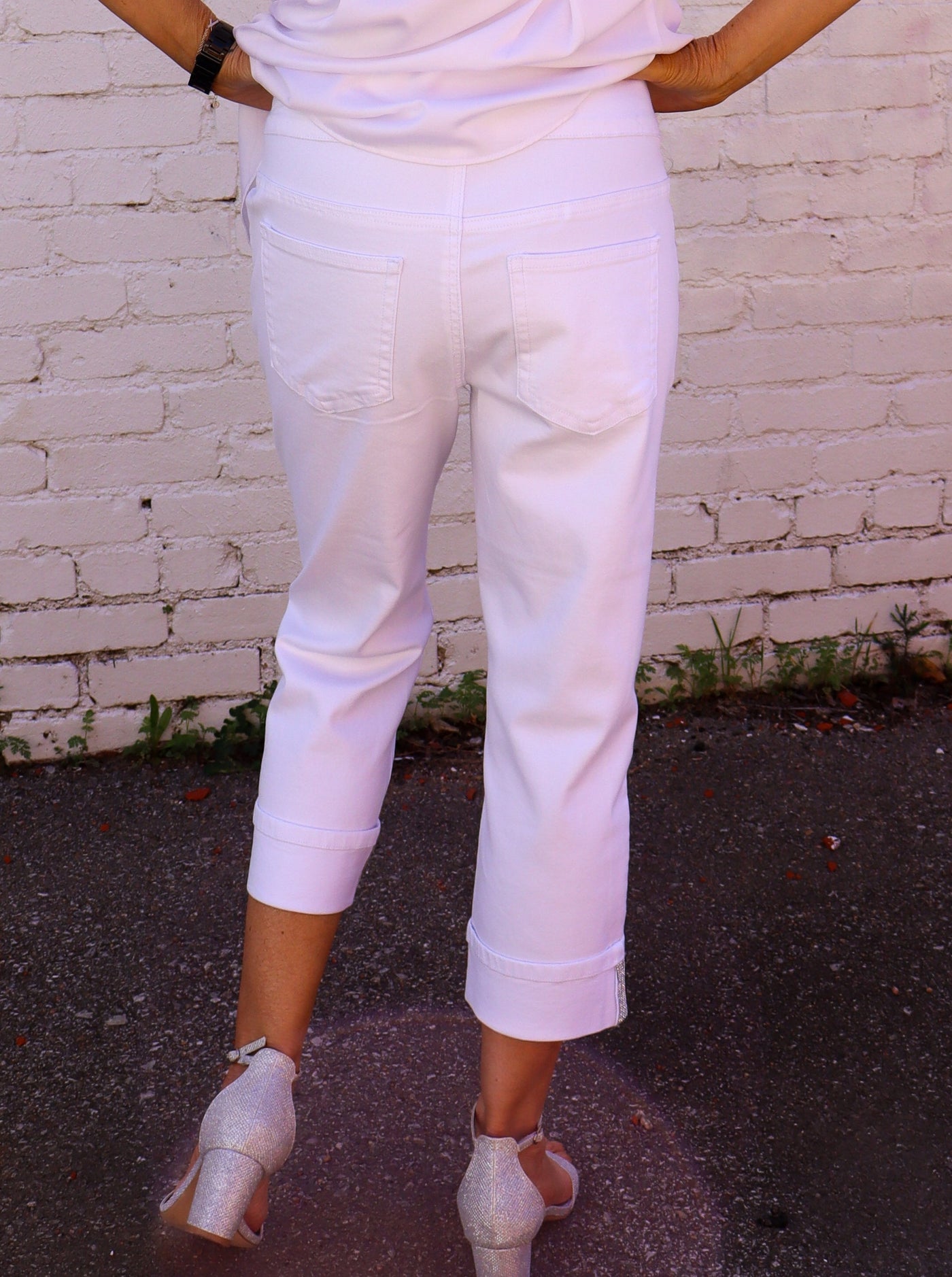 Model is wearing white pull. on jeans with sparkle details on the cuffs. Jeans are paired with a white blouse.