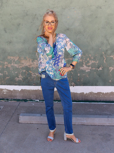 Model is wearing a dark wash blue jean with sparkle details ont the pockets and hemming of ankle. Jeans are straight leg and worn with a paisley blouse and high heels.
