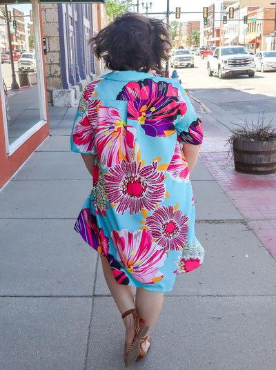 Model is wearing a multi color floral midi dress with elbow length sleeves and a v-neckline. Dress is worn with beige leather sandals.