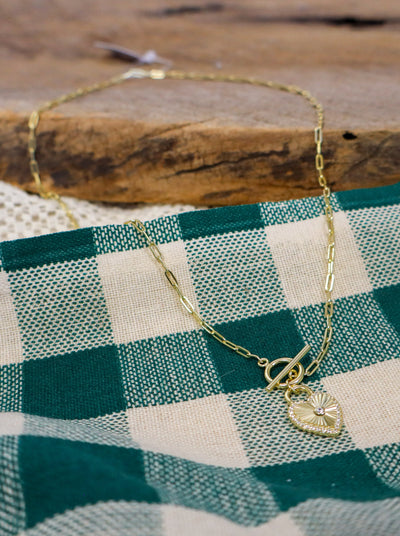 Gold chain necklace with a toggle clasp and heart pendant.