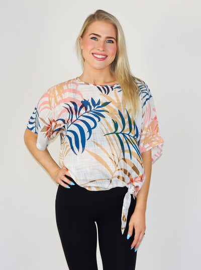 Model is wearing a multi color cotton gauze tropical printed short sleeve blouse with a tie at the hip. 