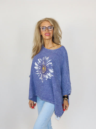 Mineral washed distressed blue oversized 3/4th sleeve top with a large flower printed in the middle. Worn with blue jeans.
