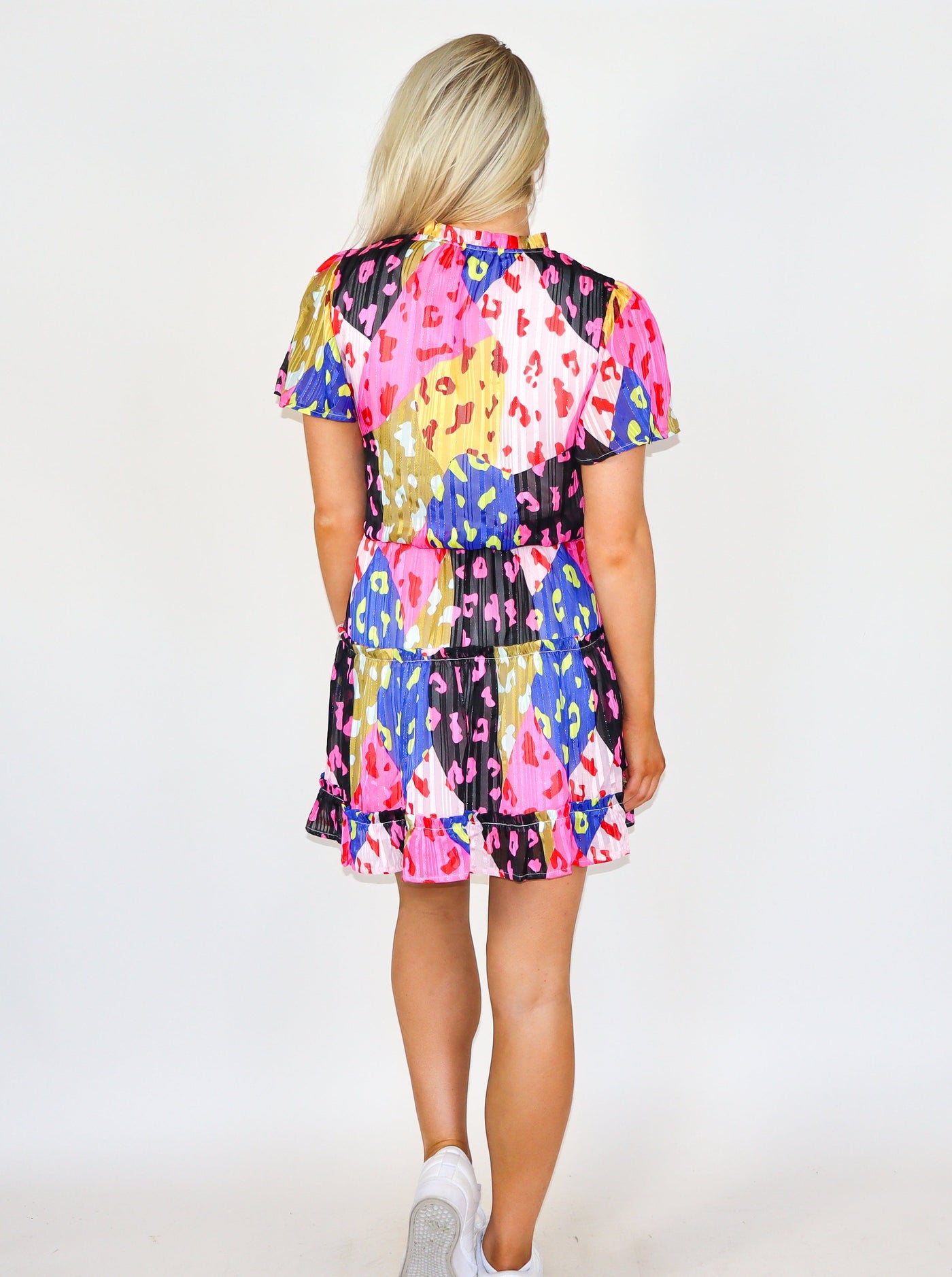 model is wearing a whimsical abstract printed midi dress with puffed sleeves, tiering, and ruffling at the skirt. Worn with white tennis shoes.