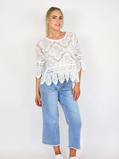 Model is wearing a see-through crochet 3/4th length sleeve top. Worn with blue jeans. 