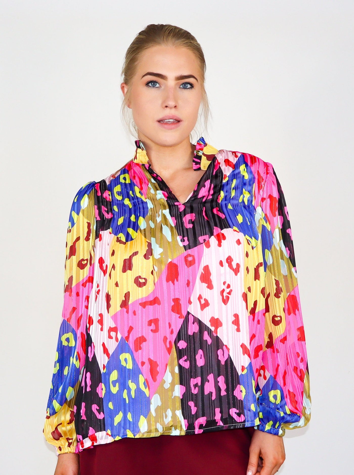 Model is wearing a prismatic printed multi color long sleeve blouse with cheetah print over lay. Split neck detail, puffed sleeves, and ruffles at the collar.