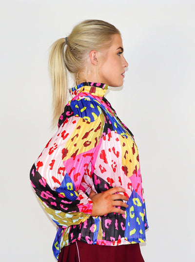 Model is wearing a prismatic printed multi color long sleeve blouse with cheetah print over lay. Split neck detail, puffed sleeves, and ruffles at the collar.