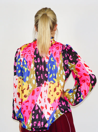 Model is wearing a prismatic printed multi color long sleeve blouse with cheetah print over lay. Split neck detail, puffed sleeves, and ruffles at the collar.