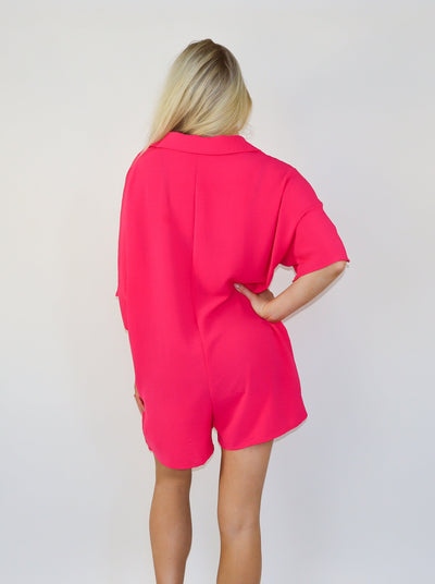 Model is wearing a neon pink oversized button collared short sleeve romper. 