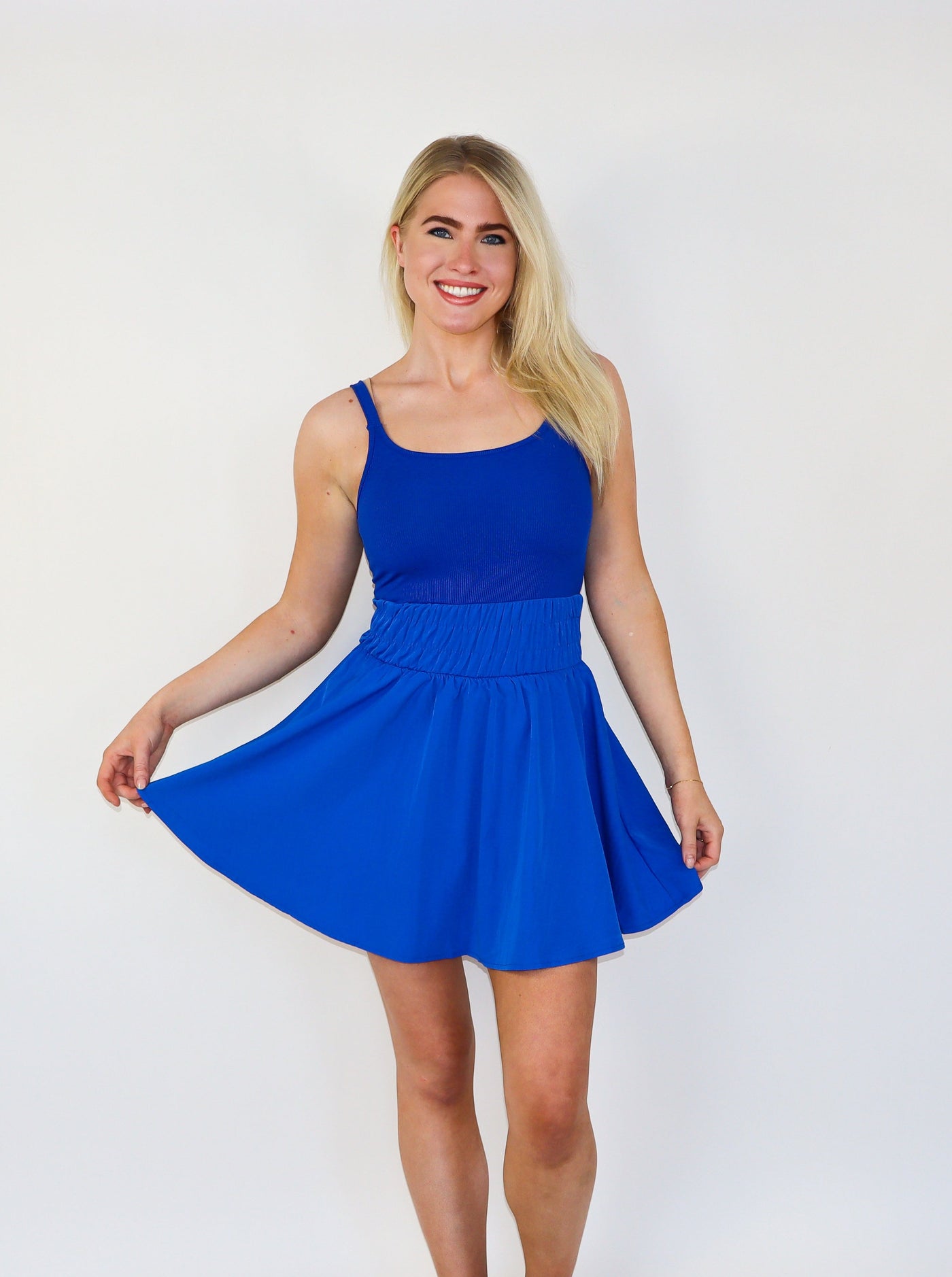 Model is wearing an electric blue mini athletic tennis dress with ruching at the waist and a flowey skirt. 