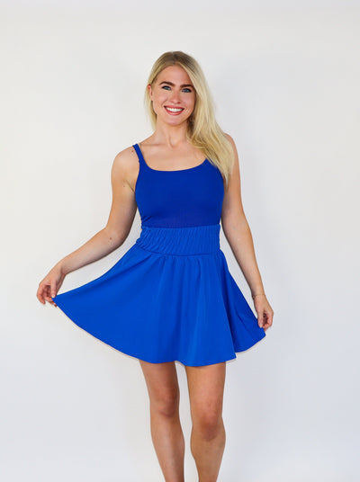 Model is wearing an electric blue mini athletic tennis dress with ruching at the waist and a flowey skirt. 