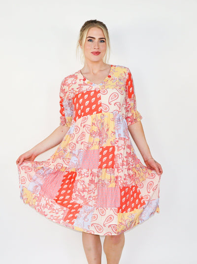 Model is wearing a orange, cream, and yellow colored patchwork paisley printed midi dress with half sleeves and a v-neck.