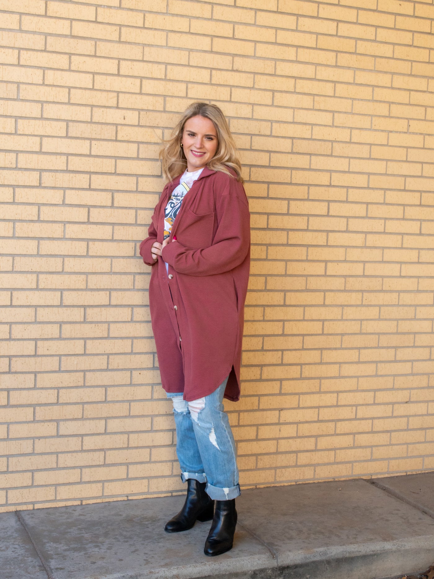 A model wearing a rose colored long shacket with a button closure. The model has it paired with a graphic tee, light wash jeans, and a black bootie.