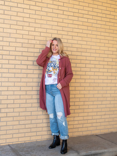 A model wearing a rose colored long shacket with a button closure. The model has it paired with a graphic tee, light wash jeans, and a black bootie.