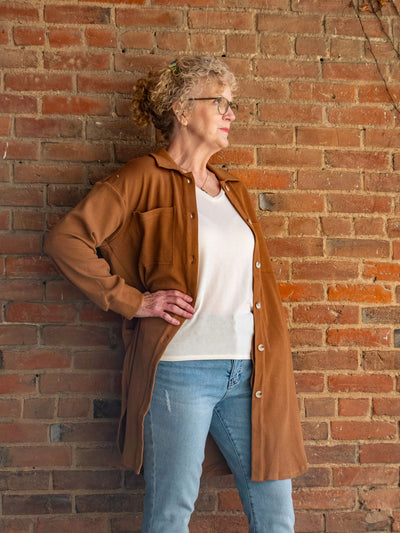 A model wearing a brown long shacket with a button closure. The model has it paired with an off white top and light wash jeans.