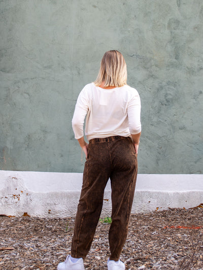A model wearing a pair of brown mineral washed pants. The model has it paired with cream v-neck top and white sneakers.