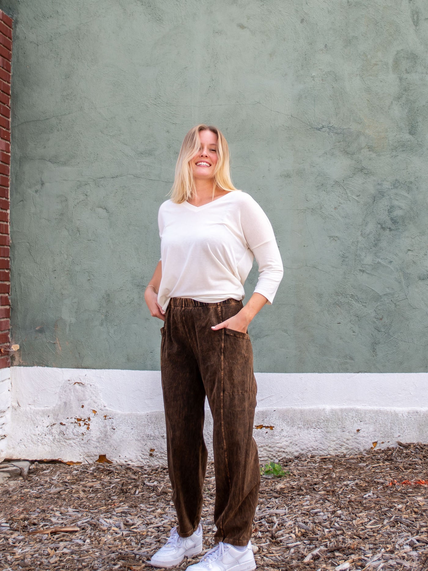 A model wearing a pair of brown mineral washed pants. The model has it paired with cream v-neck top and white sneakers.