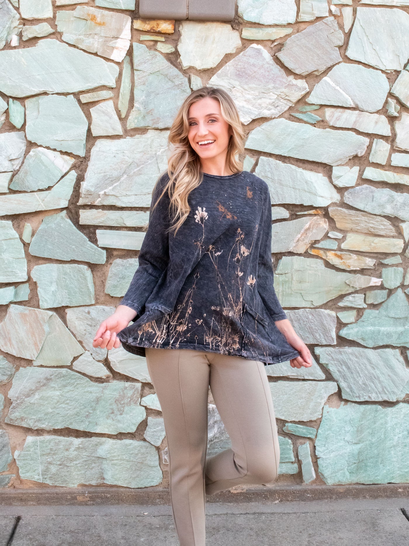 A model wearing a tunic style long sleeve top with a wildflower graphic on the front. The model has it paired with a tan pair of pants.